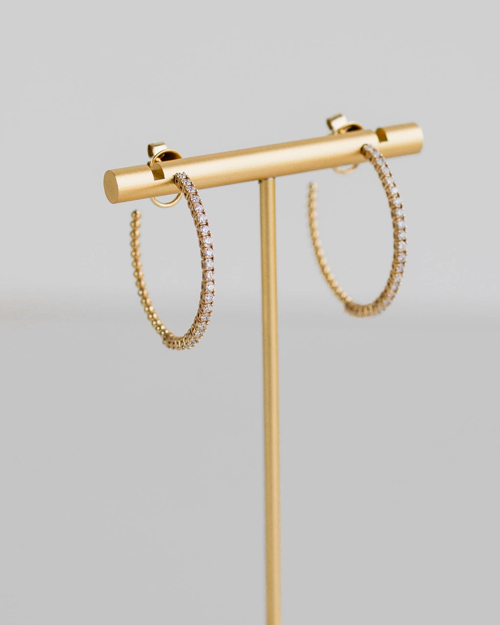 Gold earring stand with two hoop earrings on a light gray background