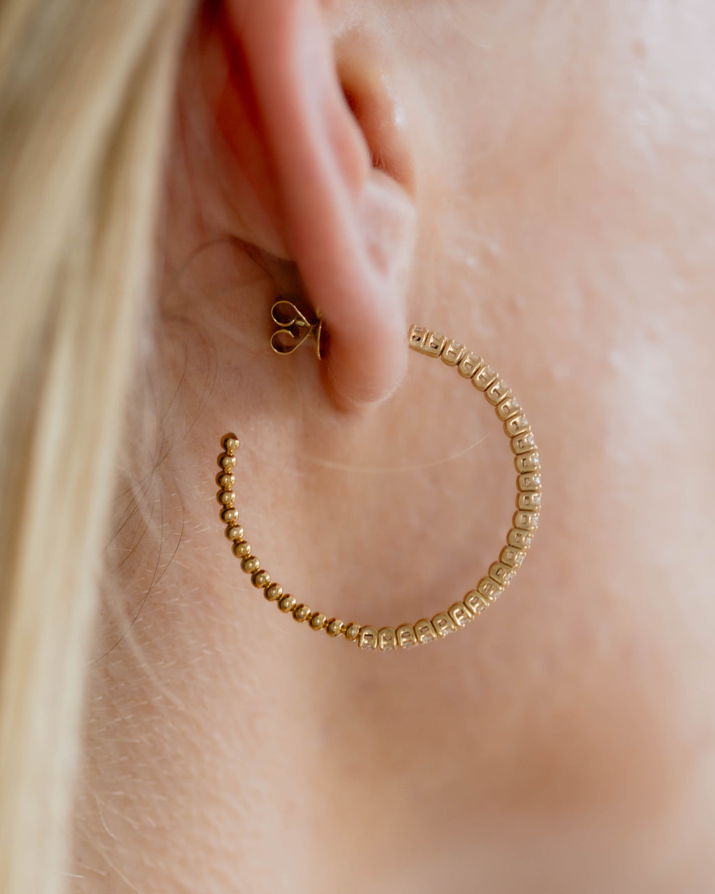 Gold hoop earring worn by a person with blonde hair.