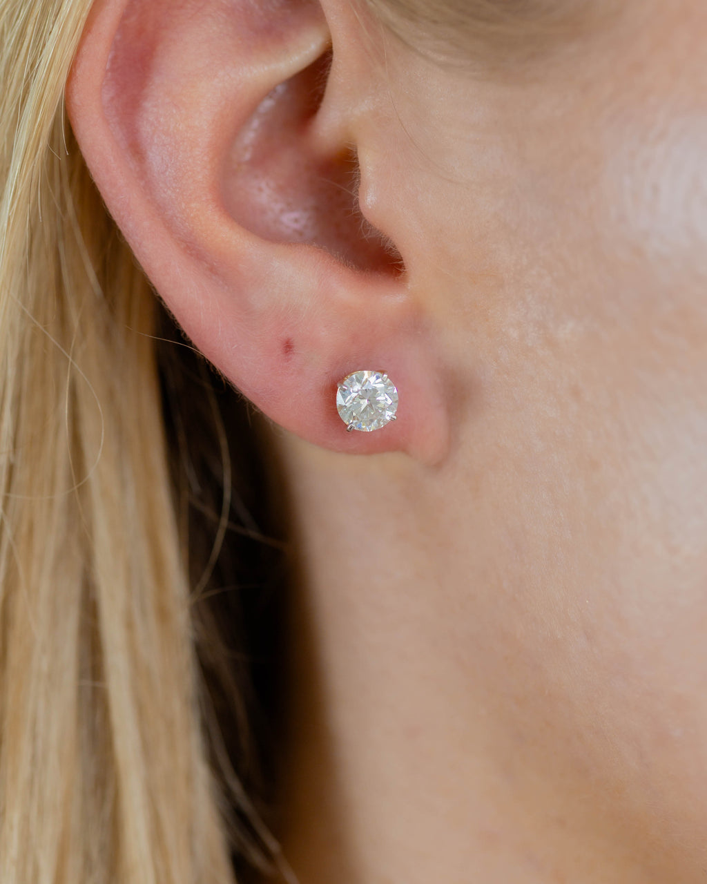 Close-up of an ear wearing a diamond stud earring with blonde hair.