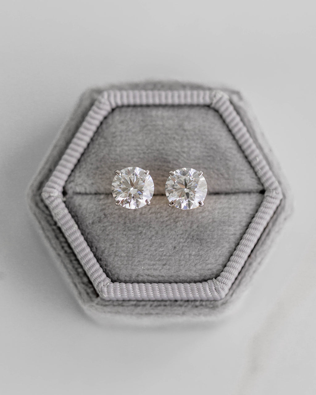 Pair of silver stud earrings in a hexagonal gray jewelry box on a light gray background