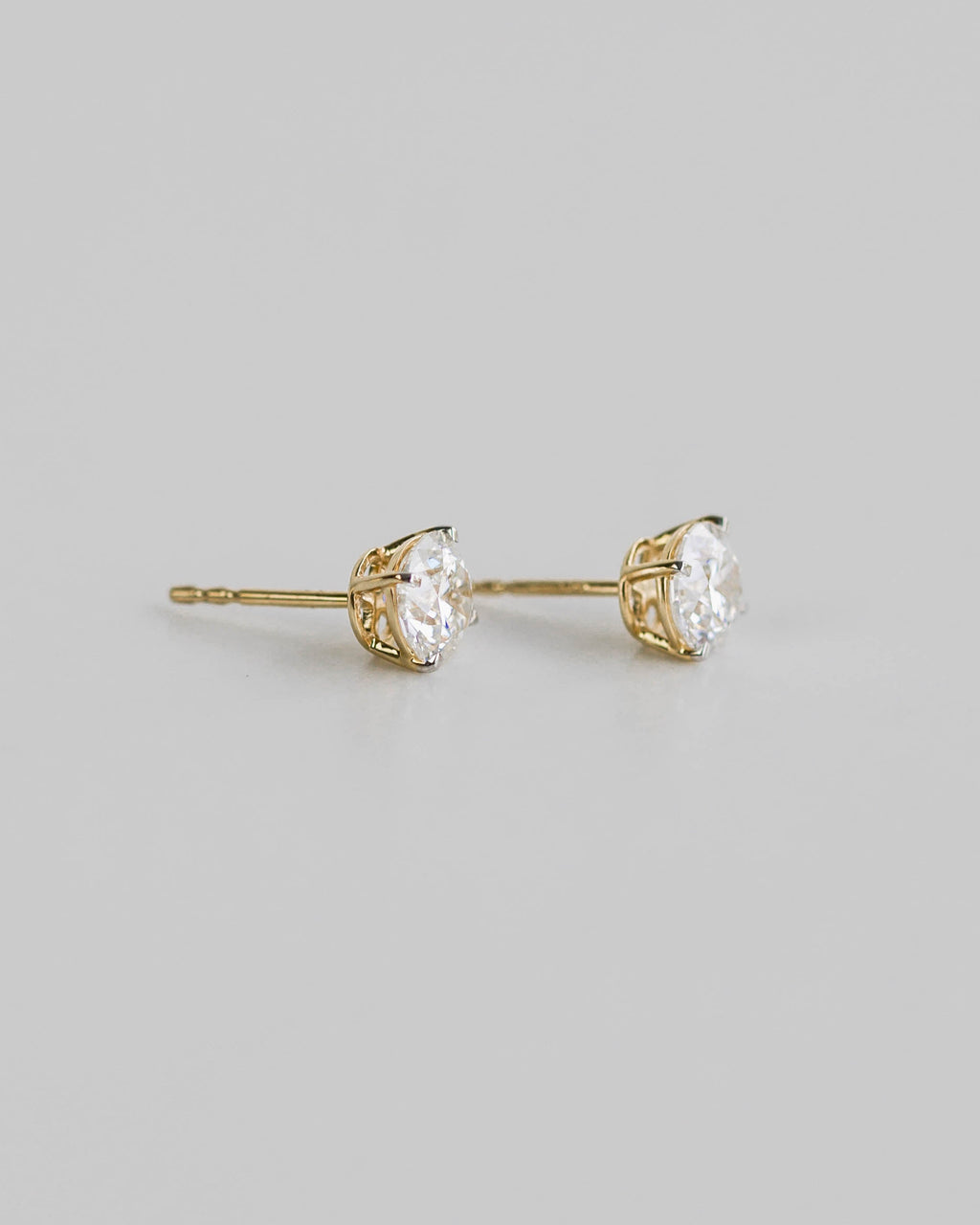 Gold earrings with clear gemstones on a light gray background