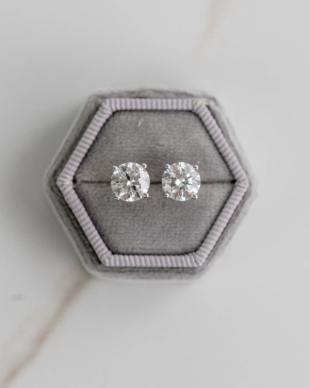 Silver stud earrings on a hexagonal gray velvet stand against a light gray background