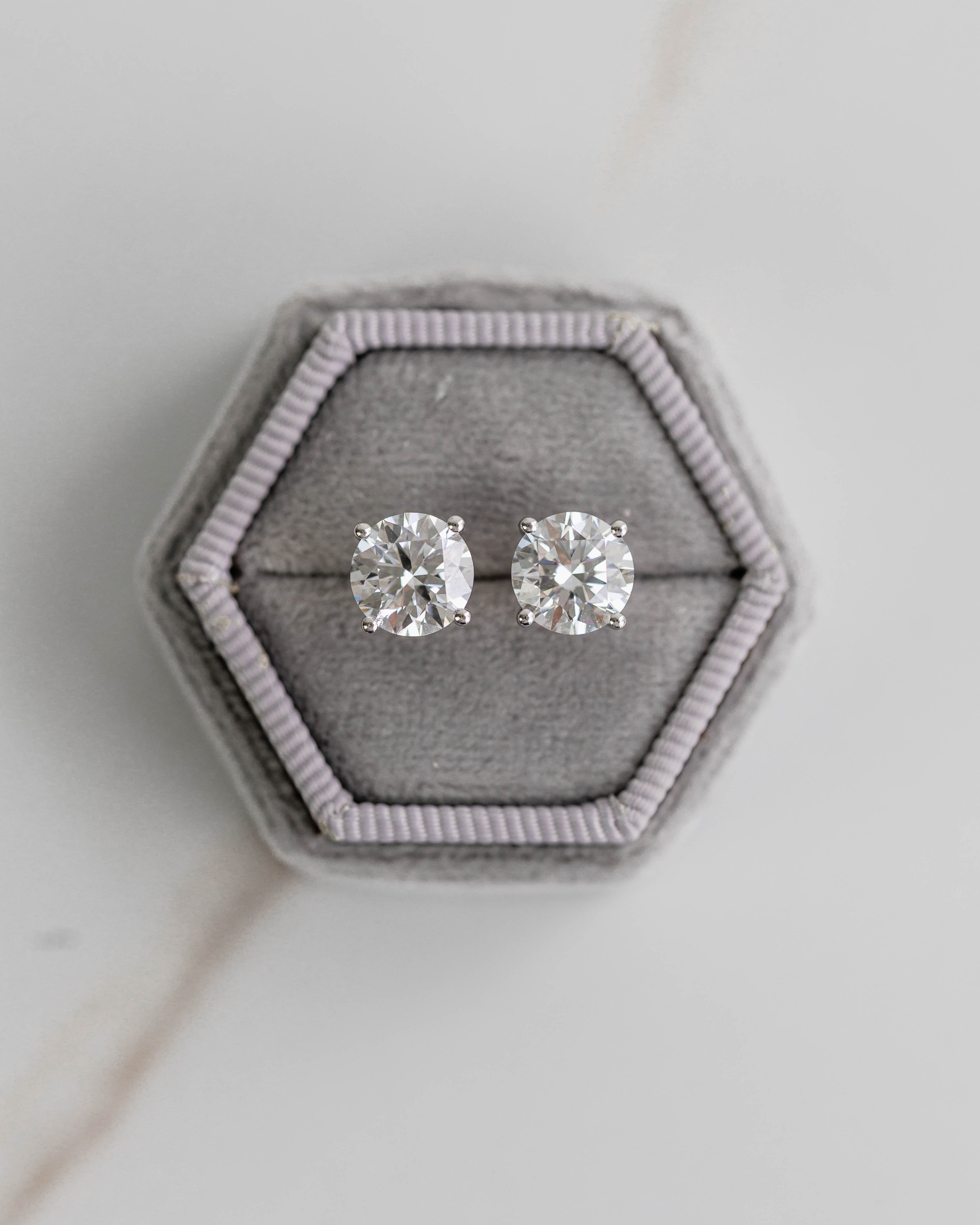Silver stud earrings on a hexagonal gray velvet stand against a light gray background