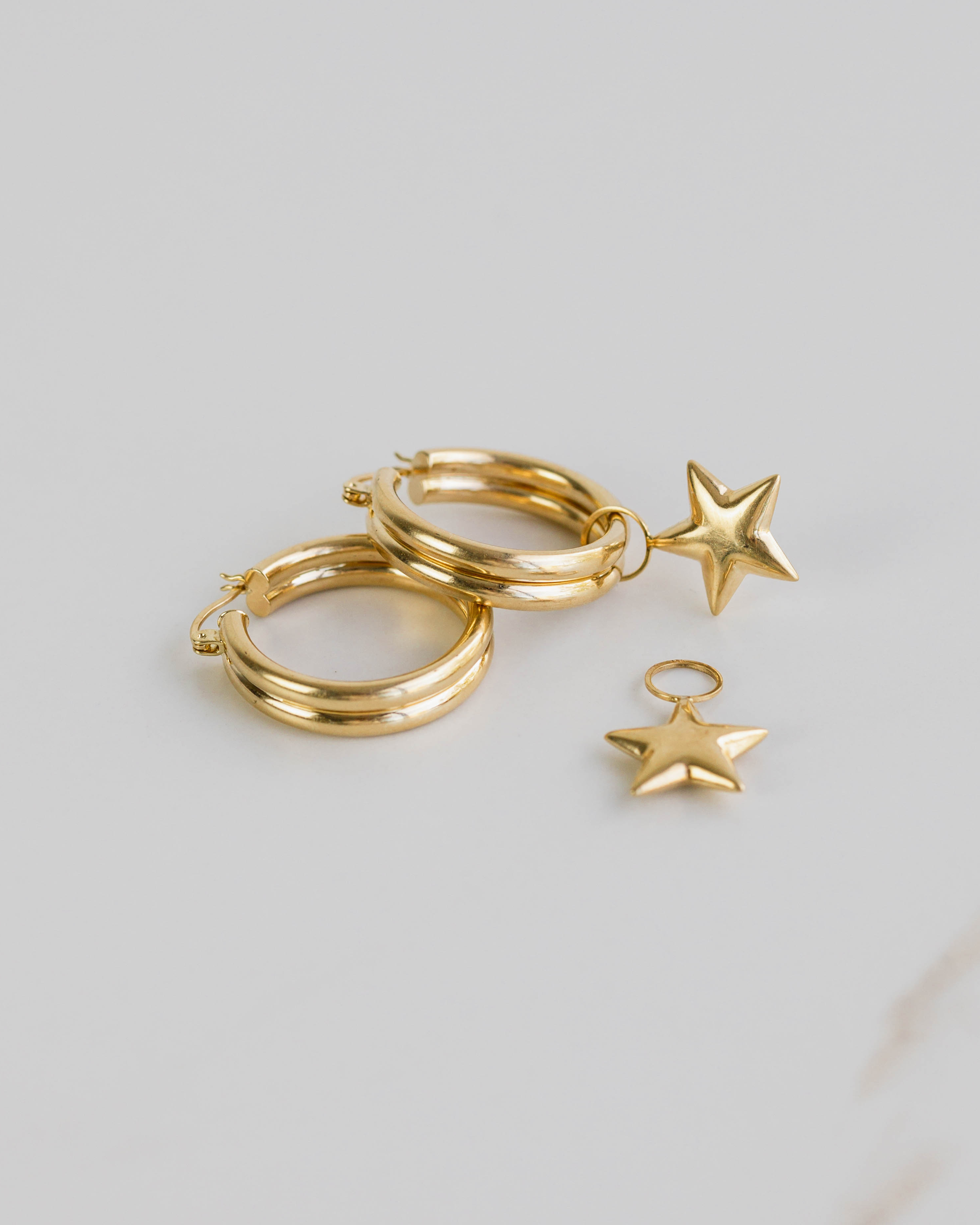 Gold hoop earrings with star charms on a light gray background