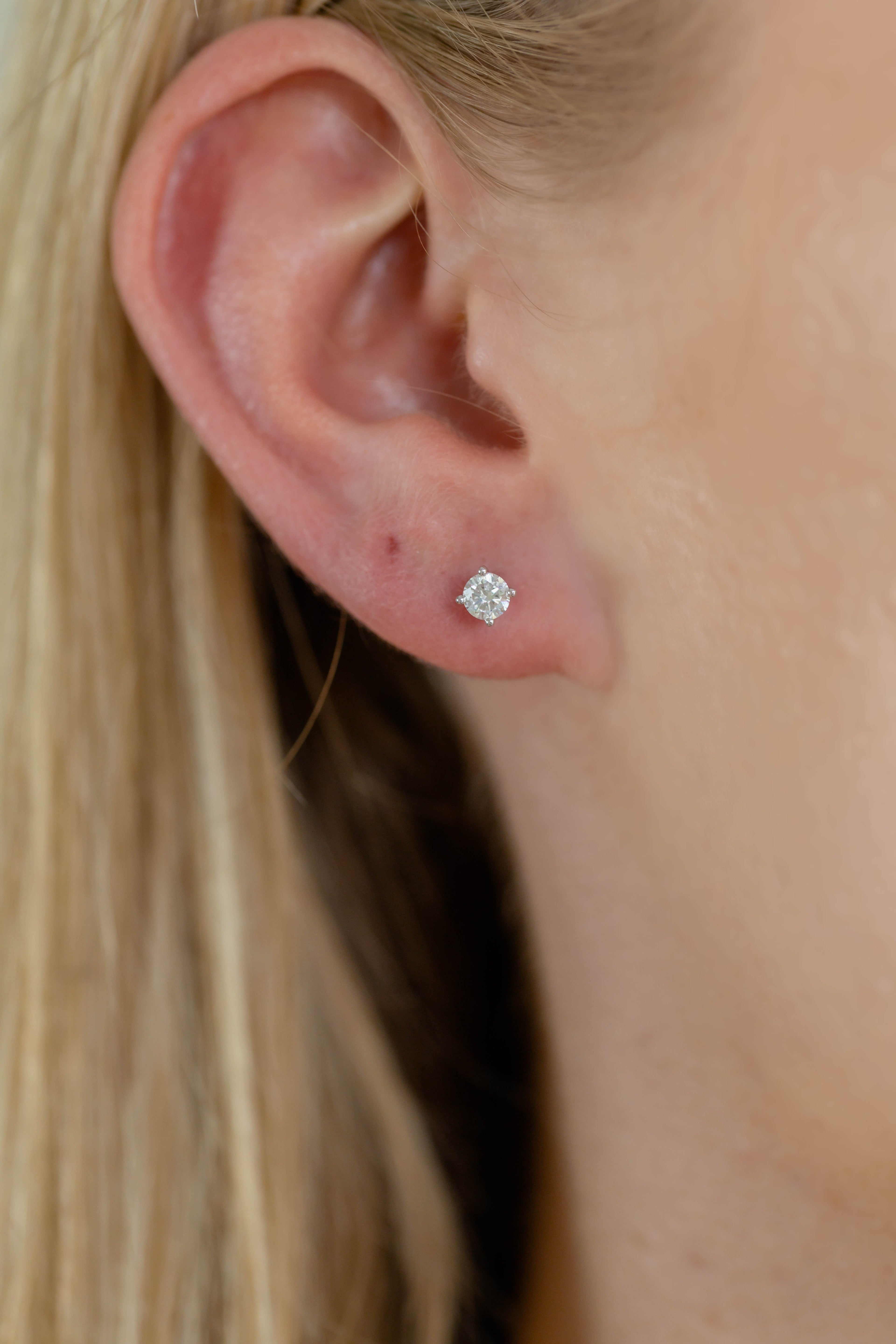 Close-up of an ear wearing a diamond stud earring with blonde hair.