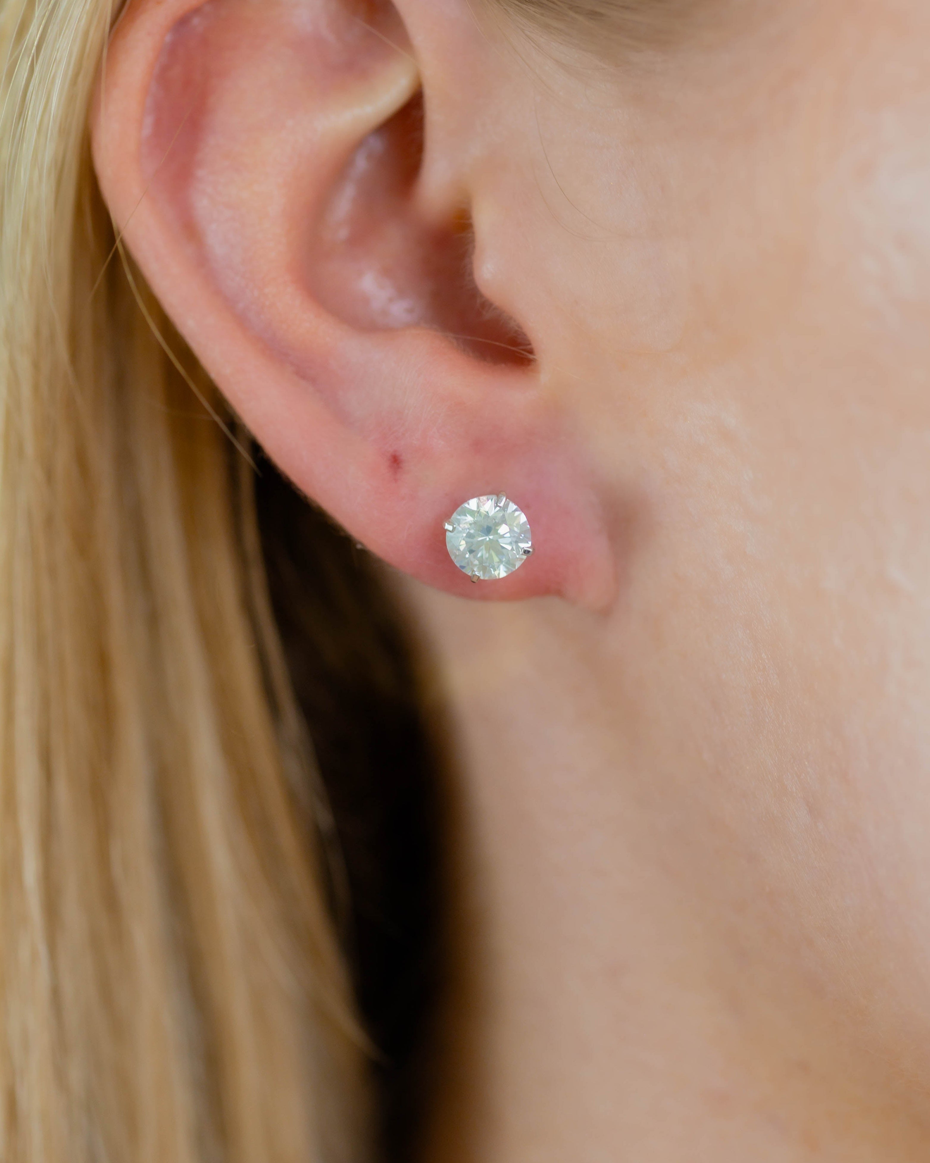 Close-up of an ear wearing a diamond stud earring with blonde hair.