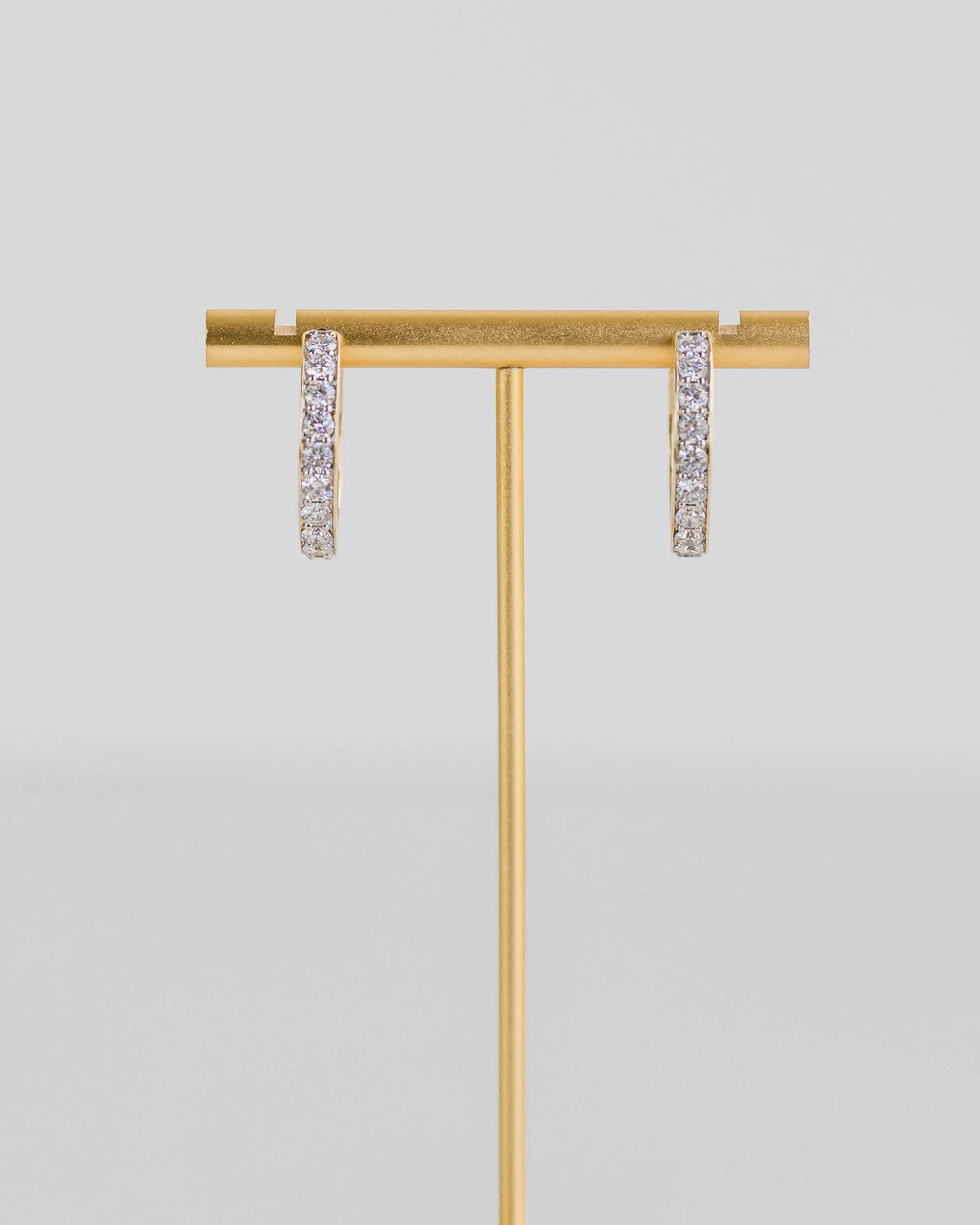 Gold earring stand with two earrings on a light gray background