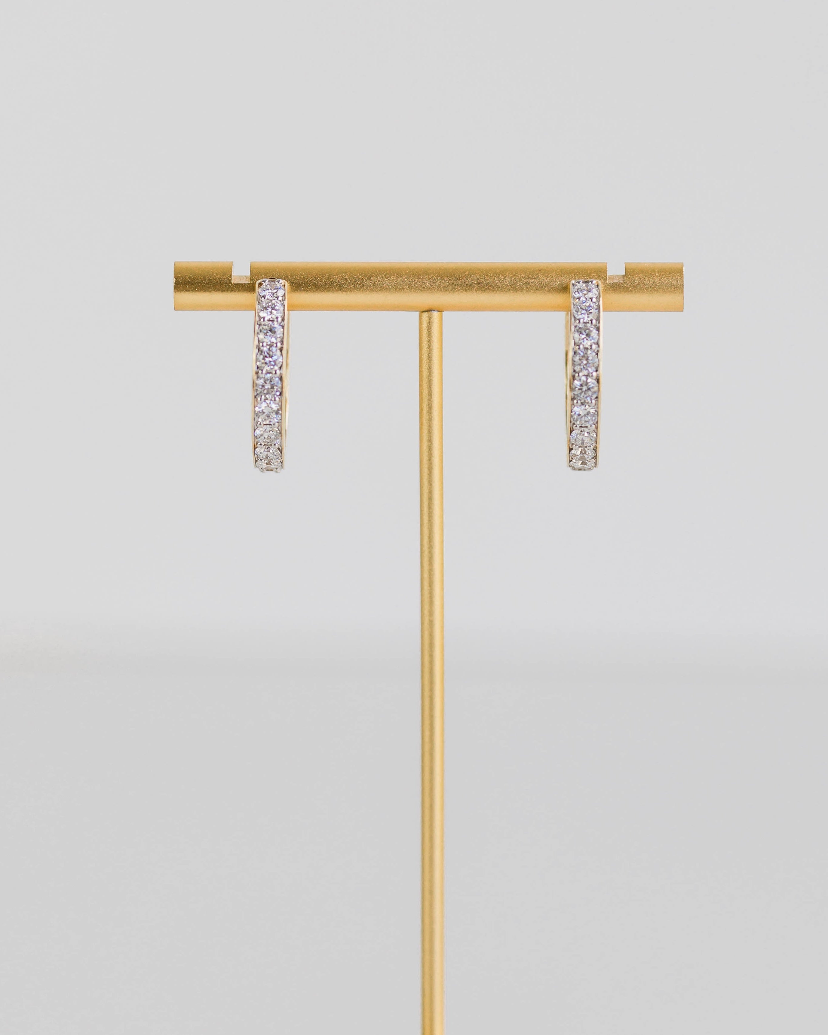 Gold earring stand with two earrings on a light gray background