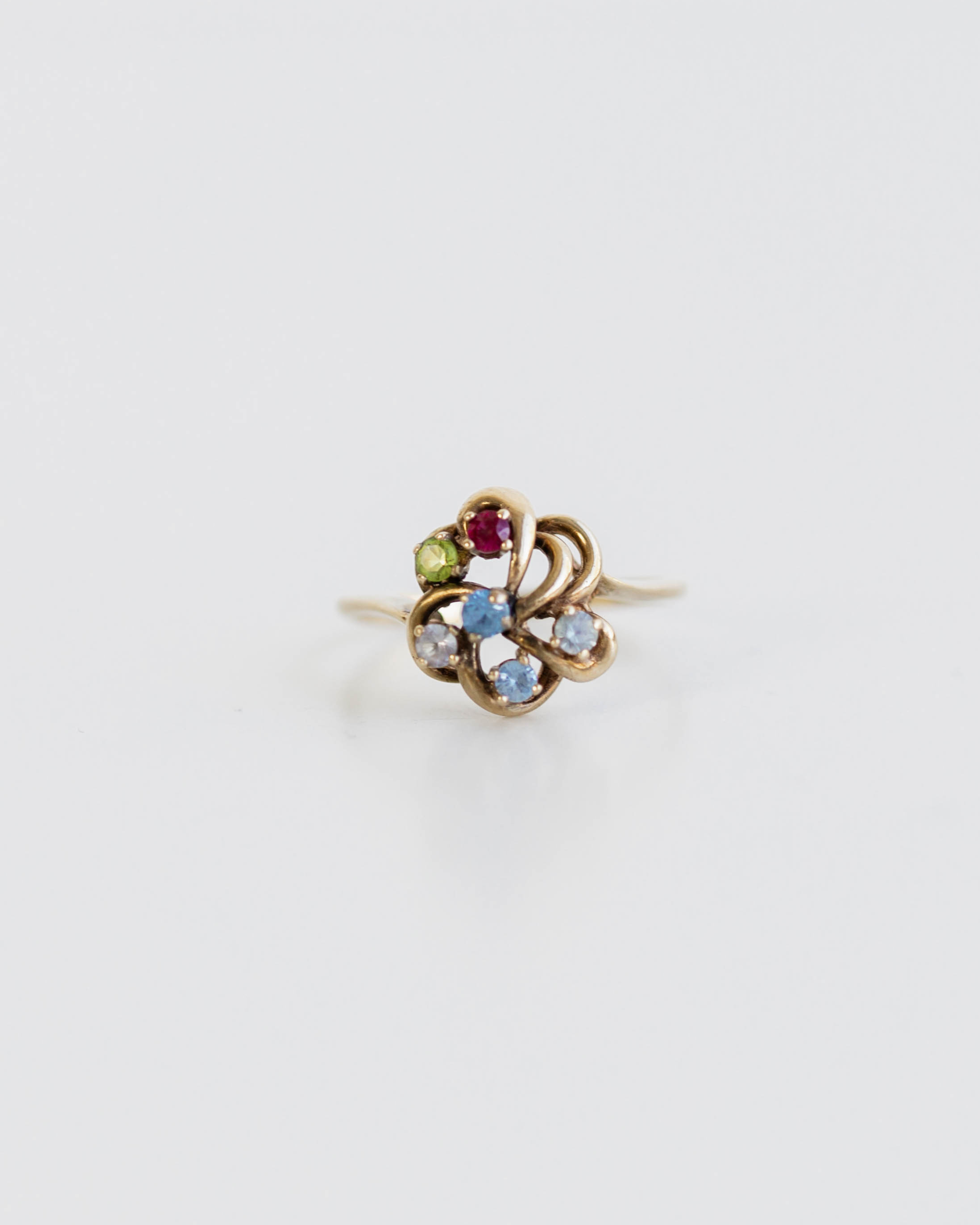 Gold ring with multicolored gemstones on a light gray background