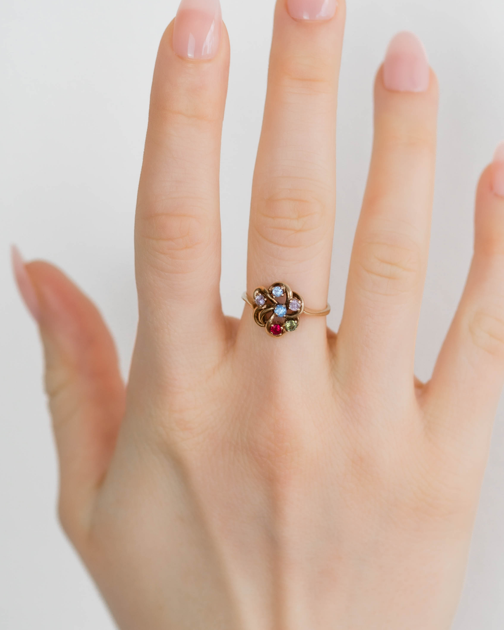 Hand wearing a ring with a colorful gemstone on a plain background