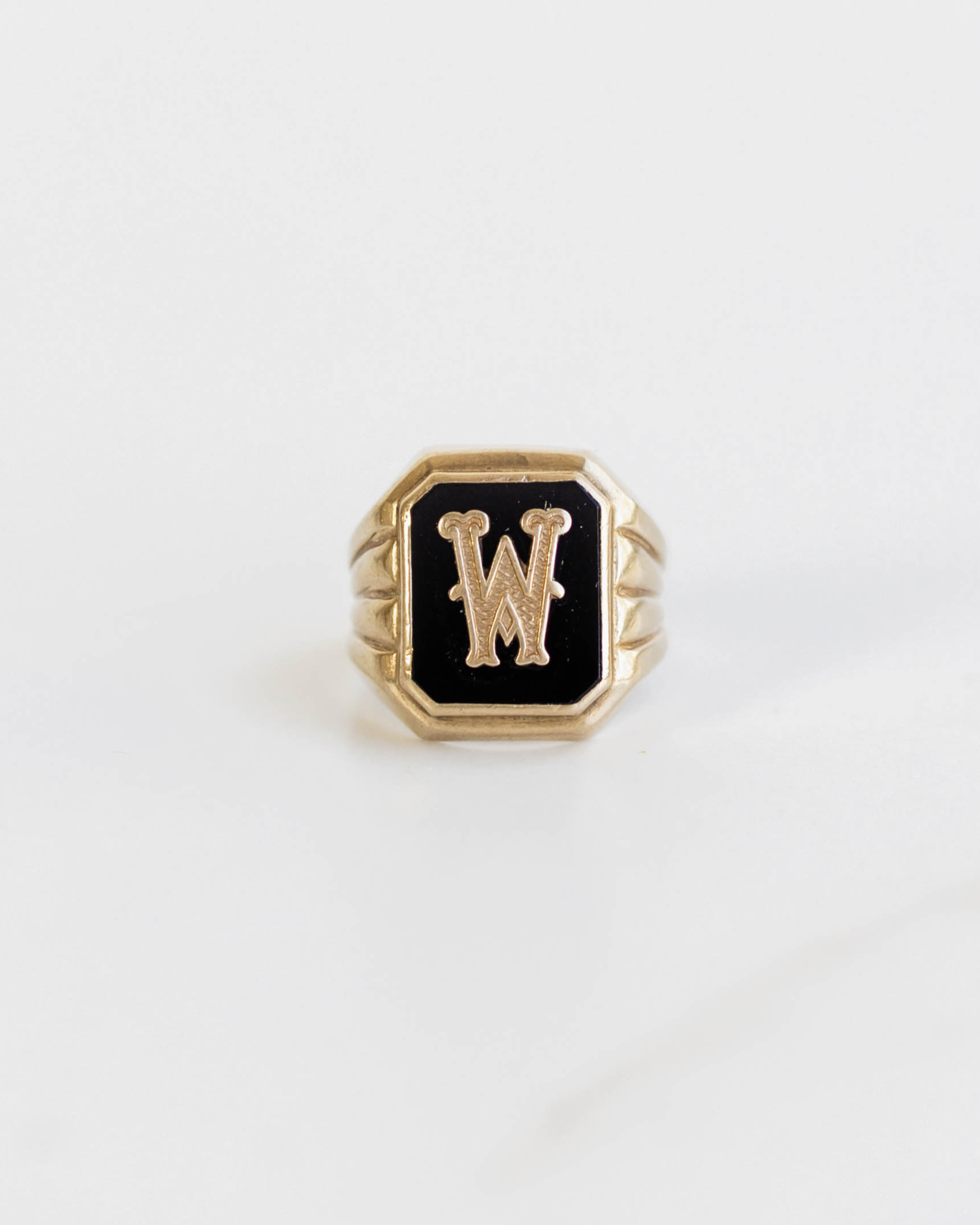 Gold ring with black octagonal stone featuring a letter 'W' on a white background