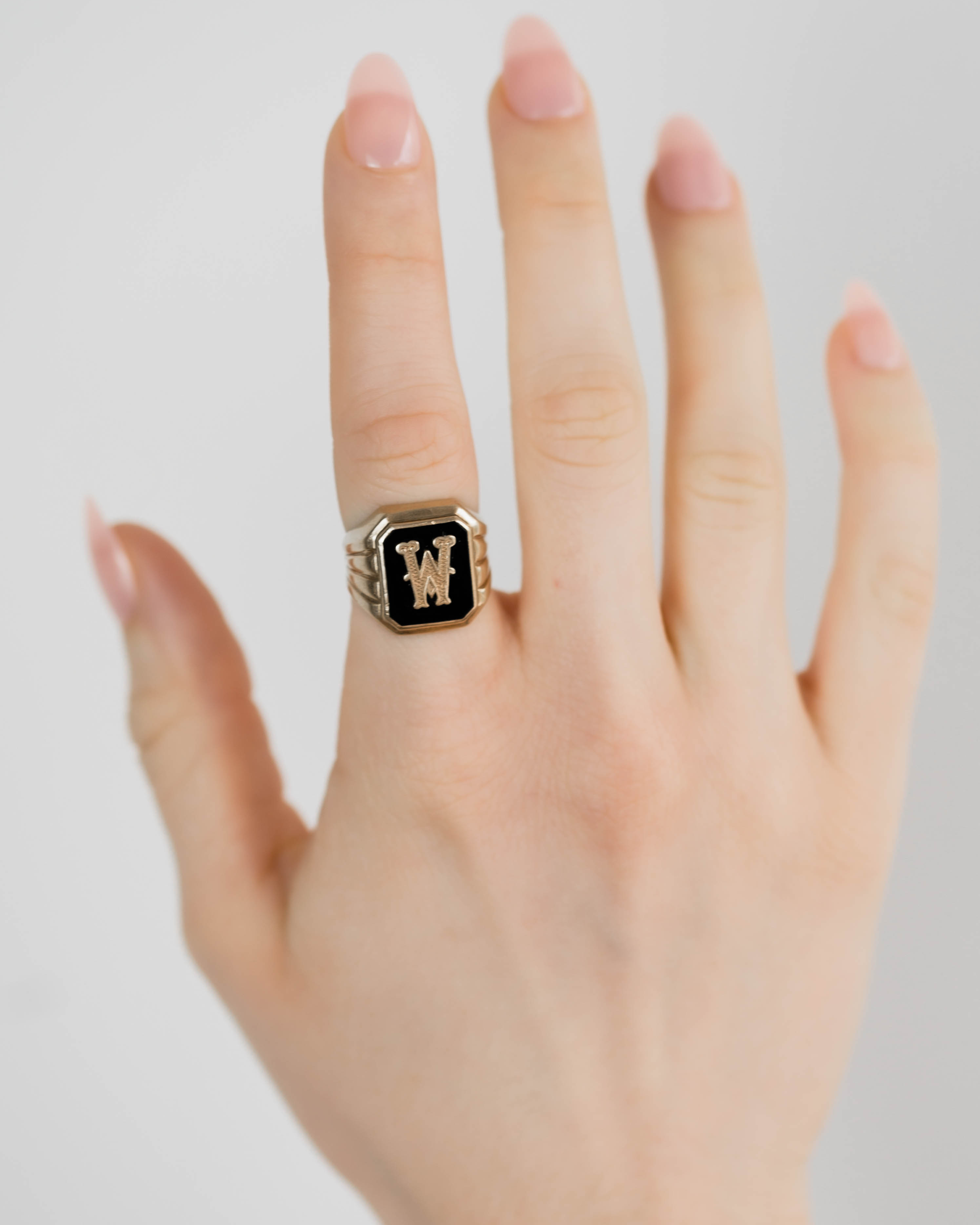 Hand wearing a gold ring with a black stone on a light gray background