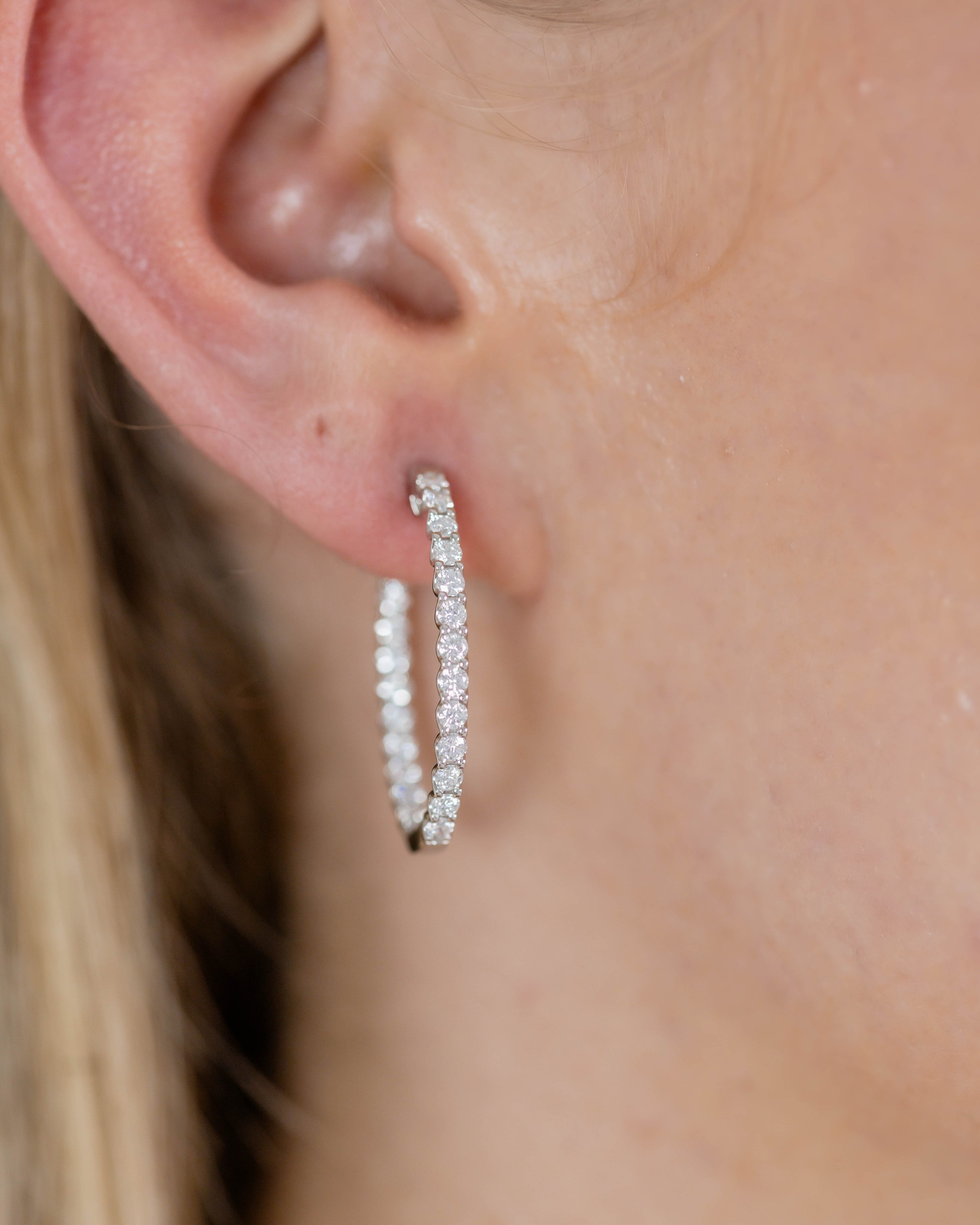 Close-up of an ear wearing a silver hoop earring with clear stones.