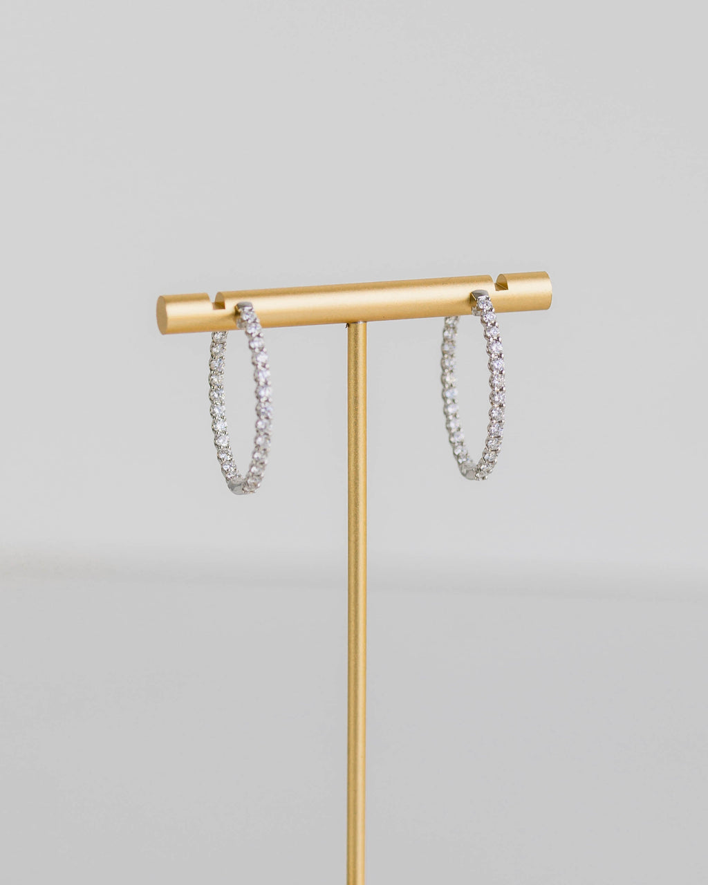 Gold jewelry stand with hexagonal base holding silver bracelets on a light gray background