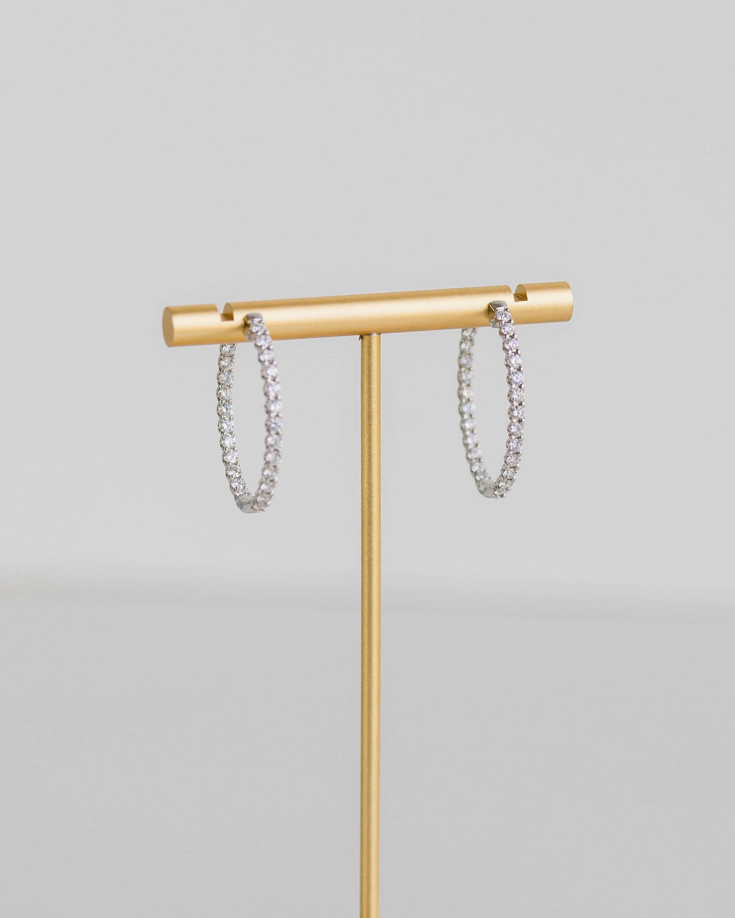 Gold jewelry stand with hexagonal base holding silver bracelets on a light gray background