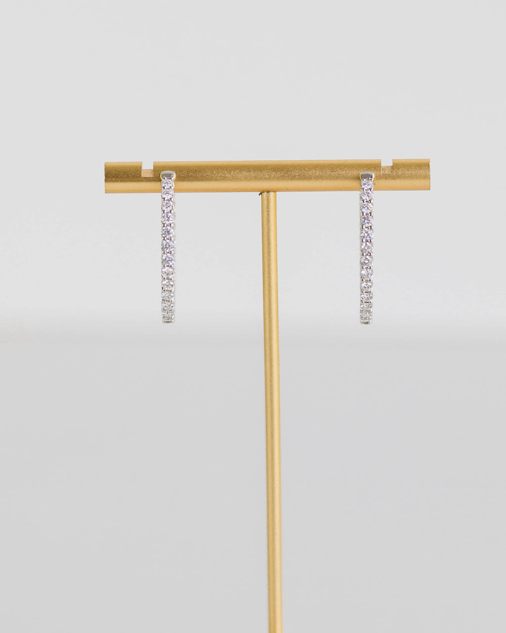 Gold jewelry stand with hexagonal base holding two pairs of earrings on a light gray background