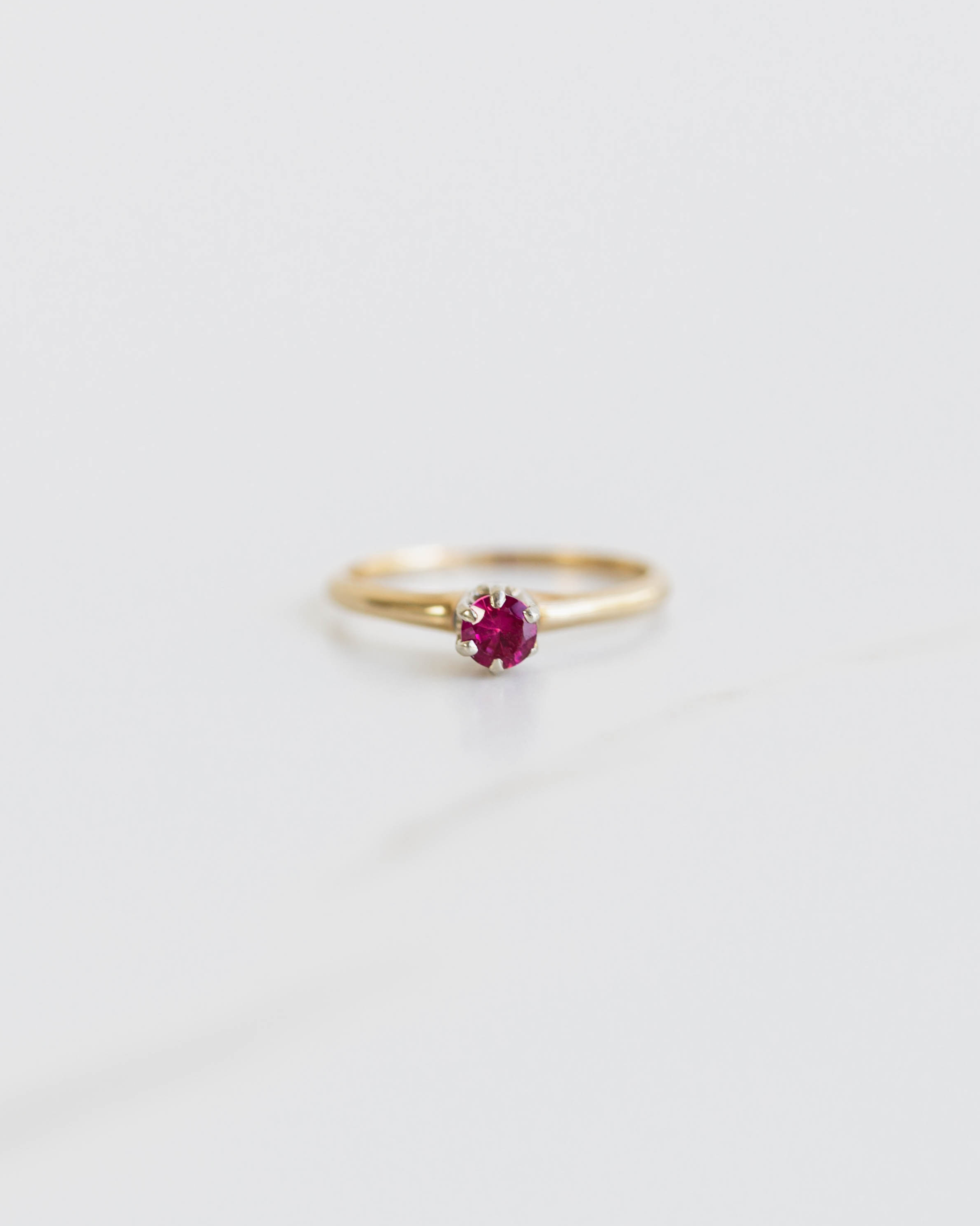 Gold ring with a red gemstone on a light gray background
