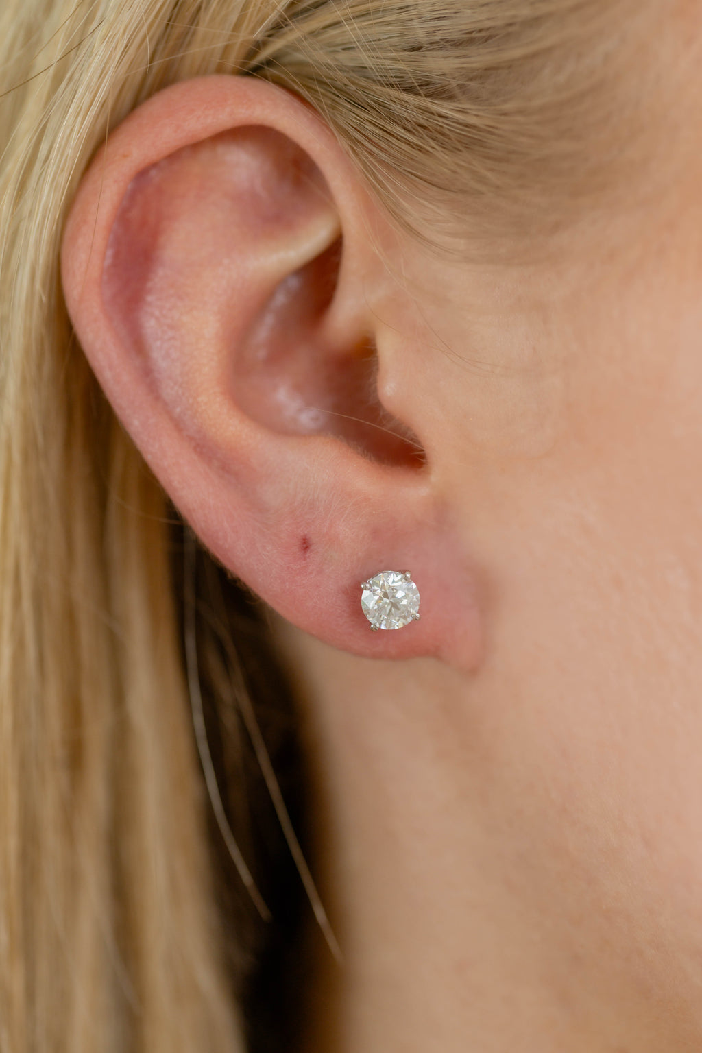 Close-up of an ear wearing a diamond stud earring with blurred background
