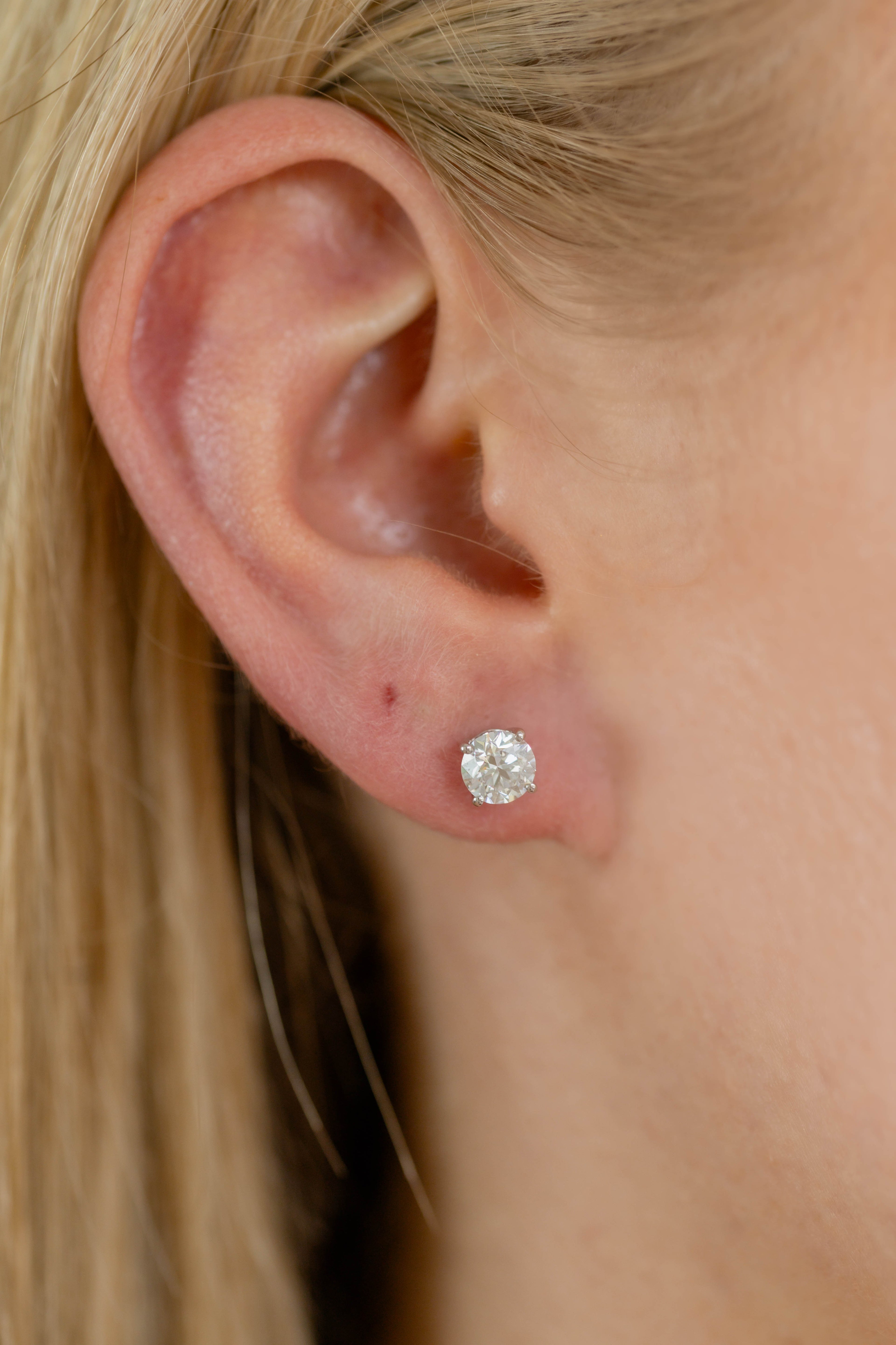 Close-up of an ear wearing a diamond stud earring with blurred background