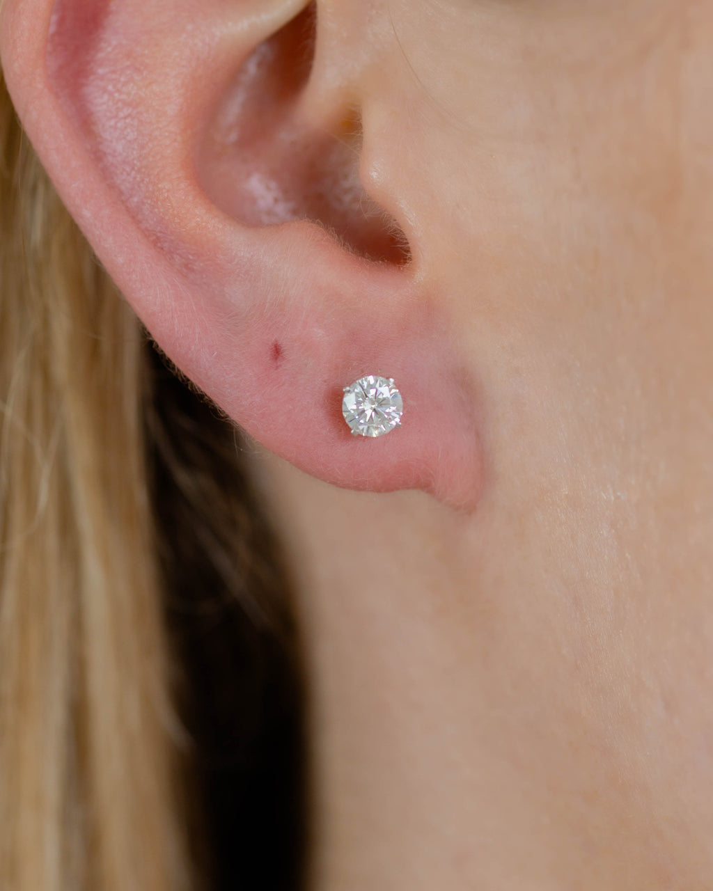 Close-up of an ear wearing a diamond stud earring with blonde hair.