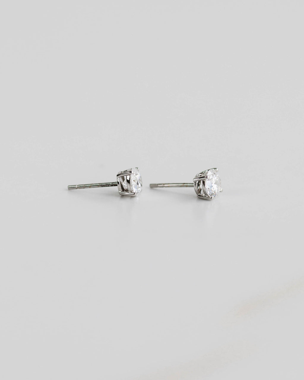 Pair of silver stud earrings with clear gemstones on a light gray background