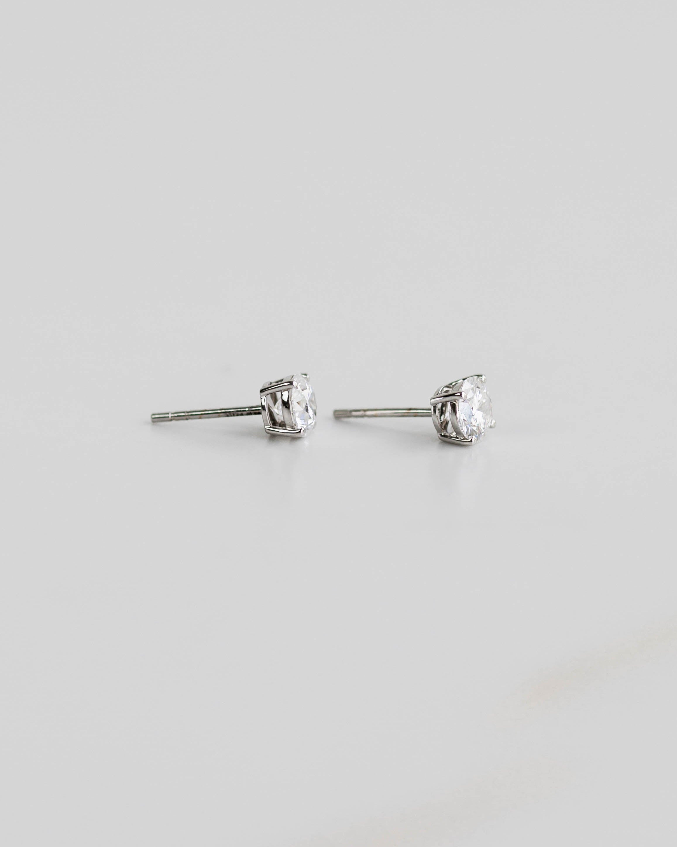 Pair of silver stud earrings with clear gemstones on a light gray background