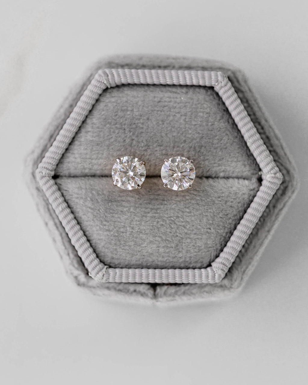 Pair of silver earrings in a hexagonal gray velvet box on a light gray background