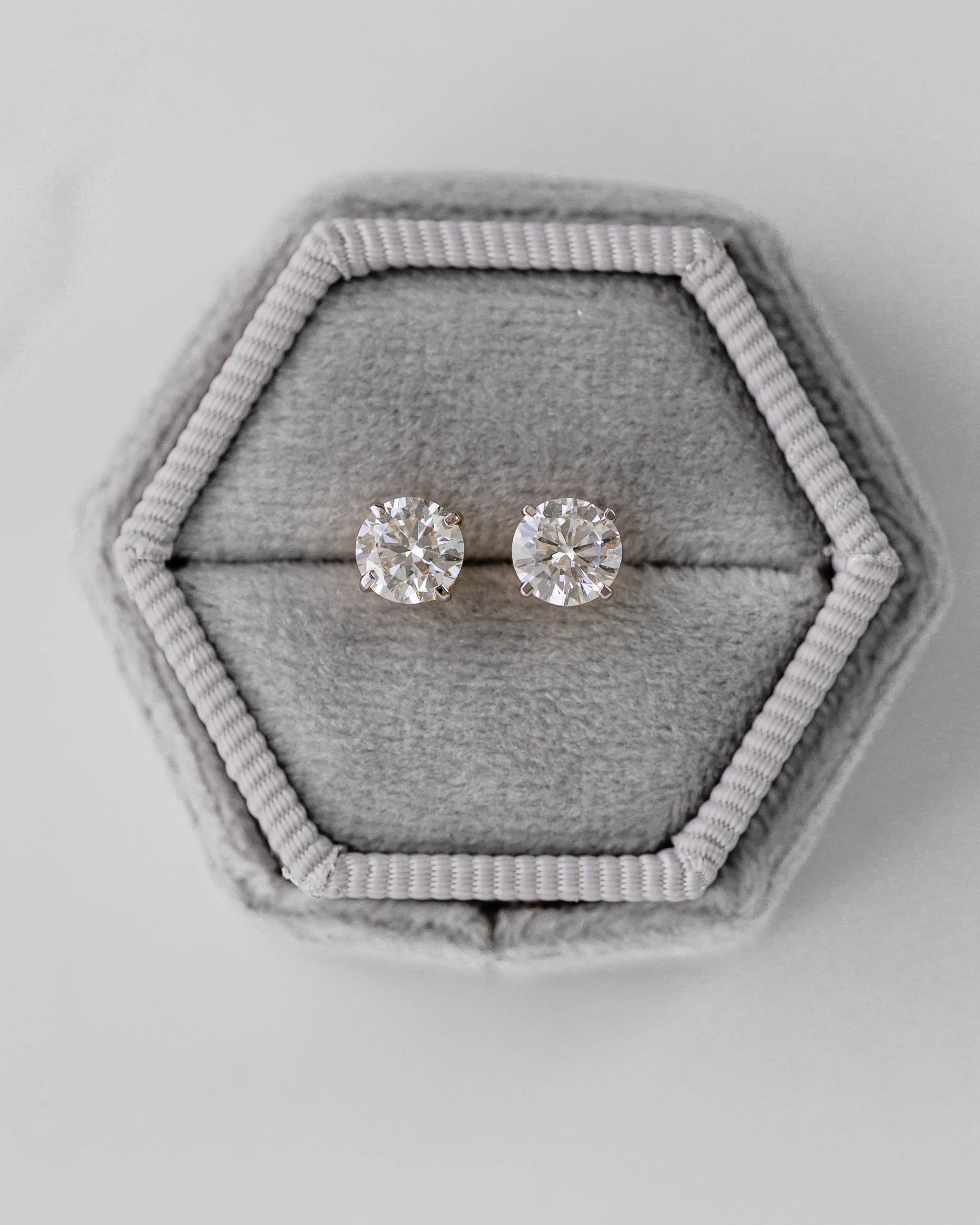 Pair of silver earrings in a hexagonal gray velvet box on a light gray background