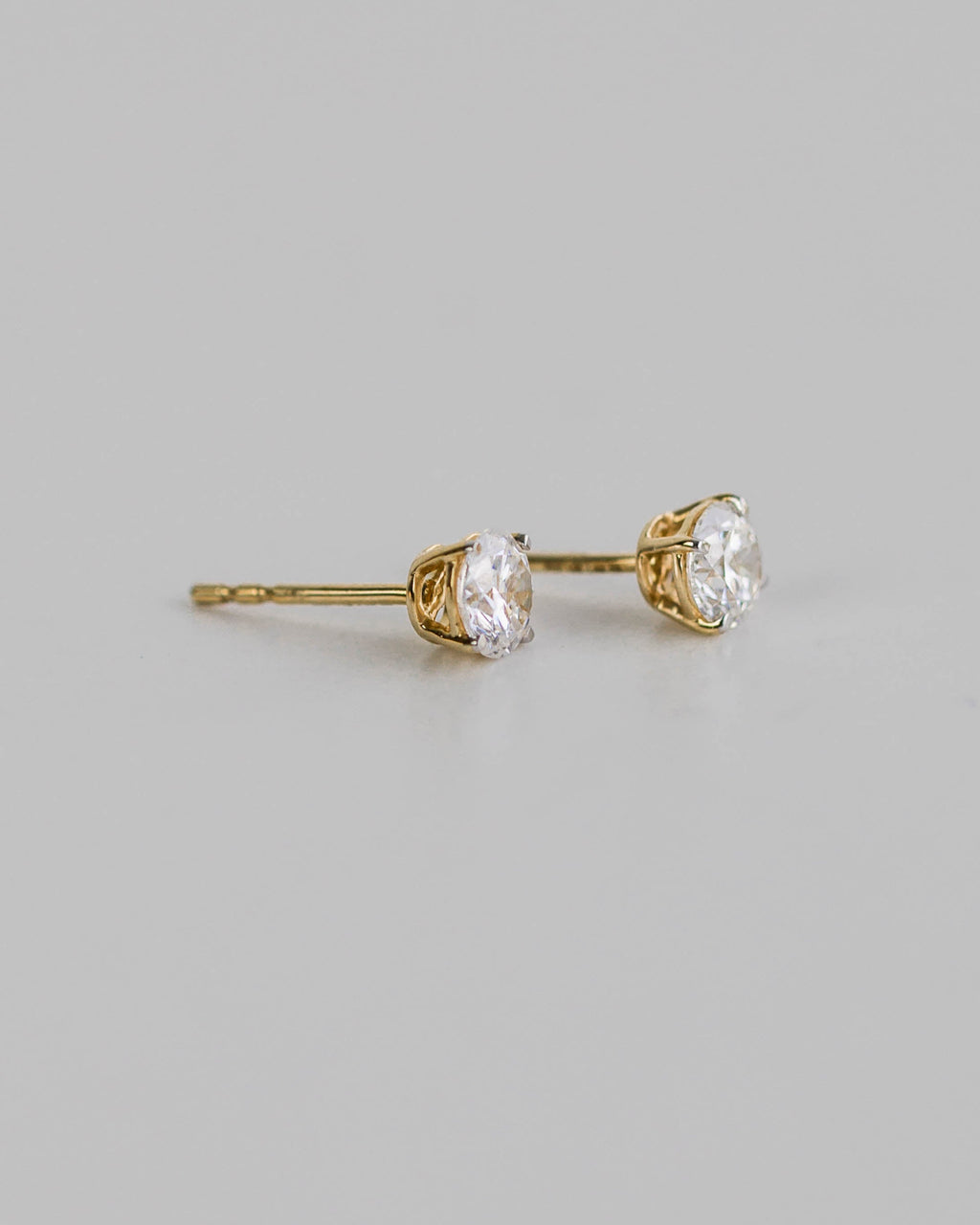 Gold stud earrings with clear gemstones on a gray background