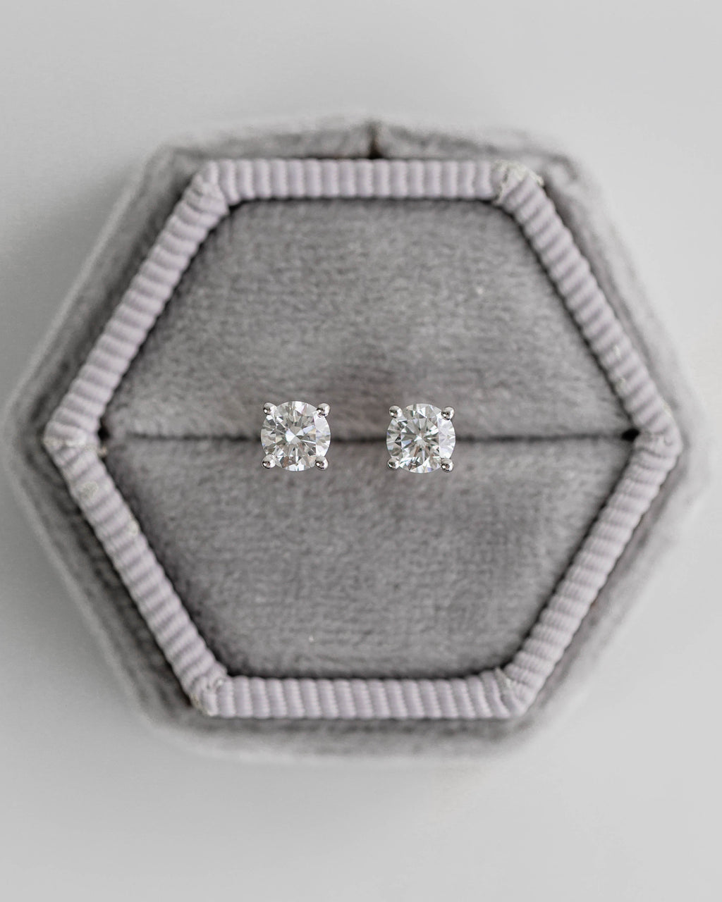 Silver stud earrings in a hexagonal gray jewelry box on a light gray background