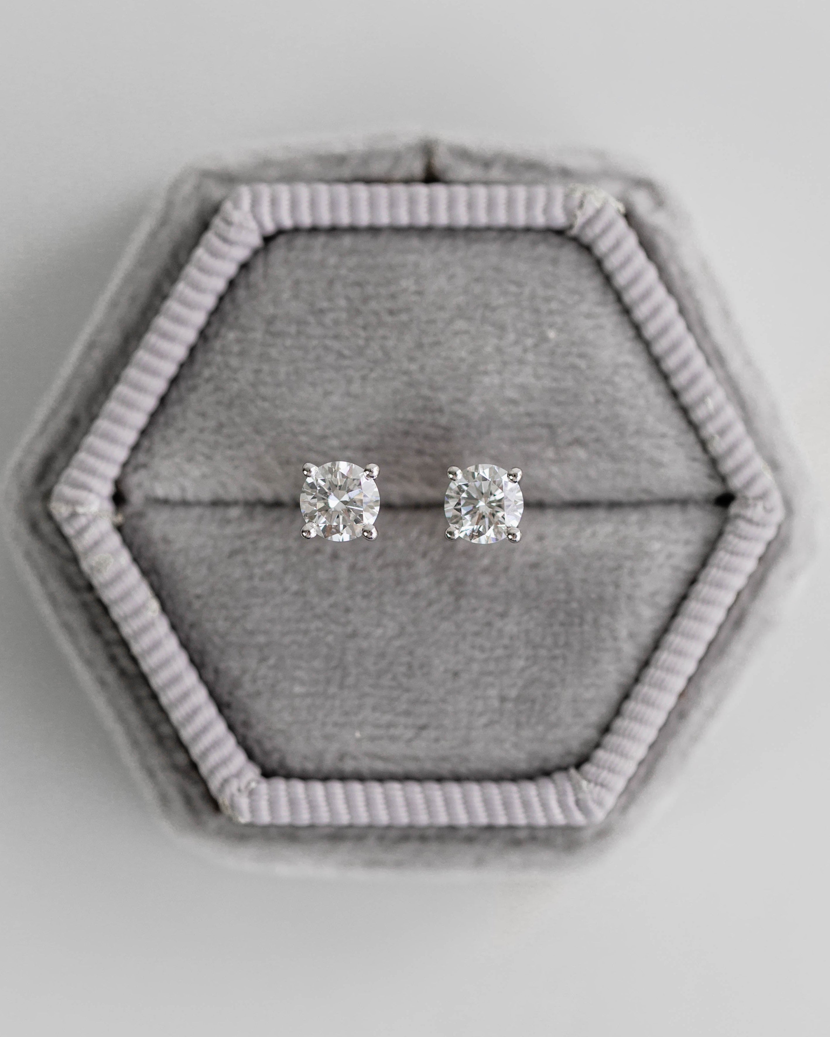 Silver stud earrings in a hexagonal gray jewelry box on a light gray background