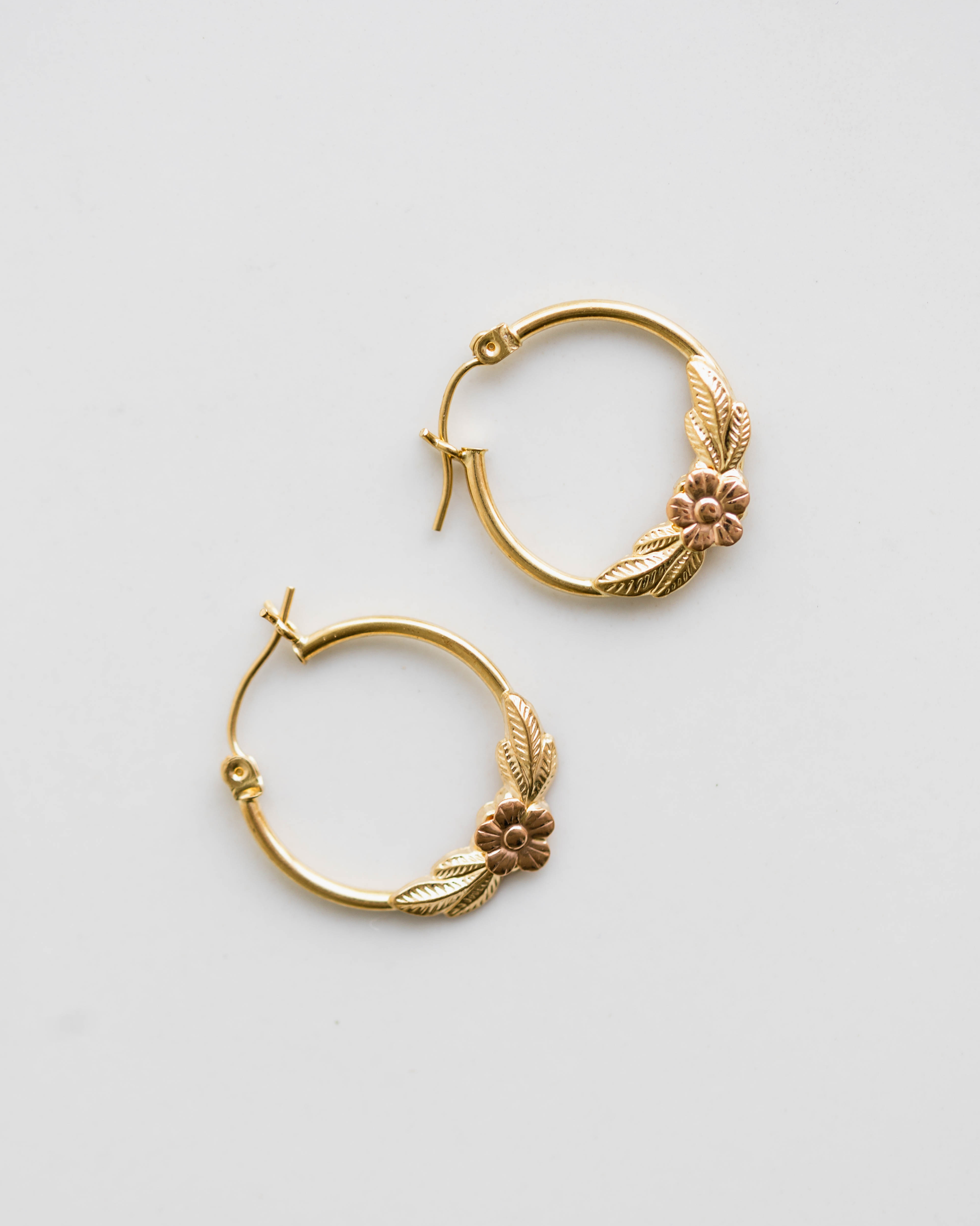 Gold hoop earrings with floral designs on a light gray background