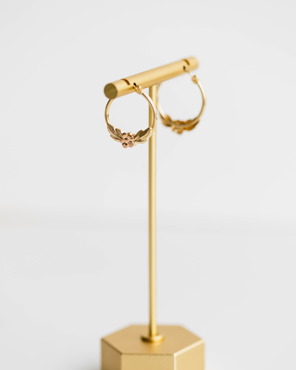 Gold hoop earrings on a matching gold stand against a white background