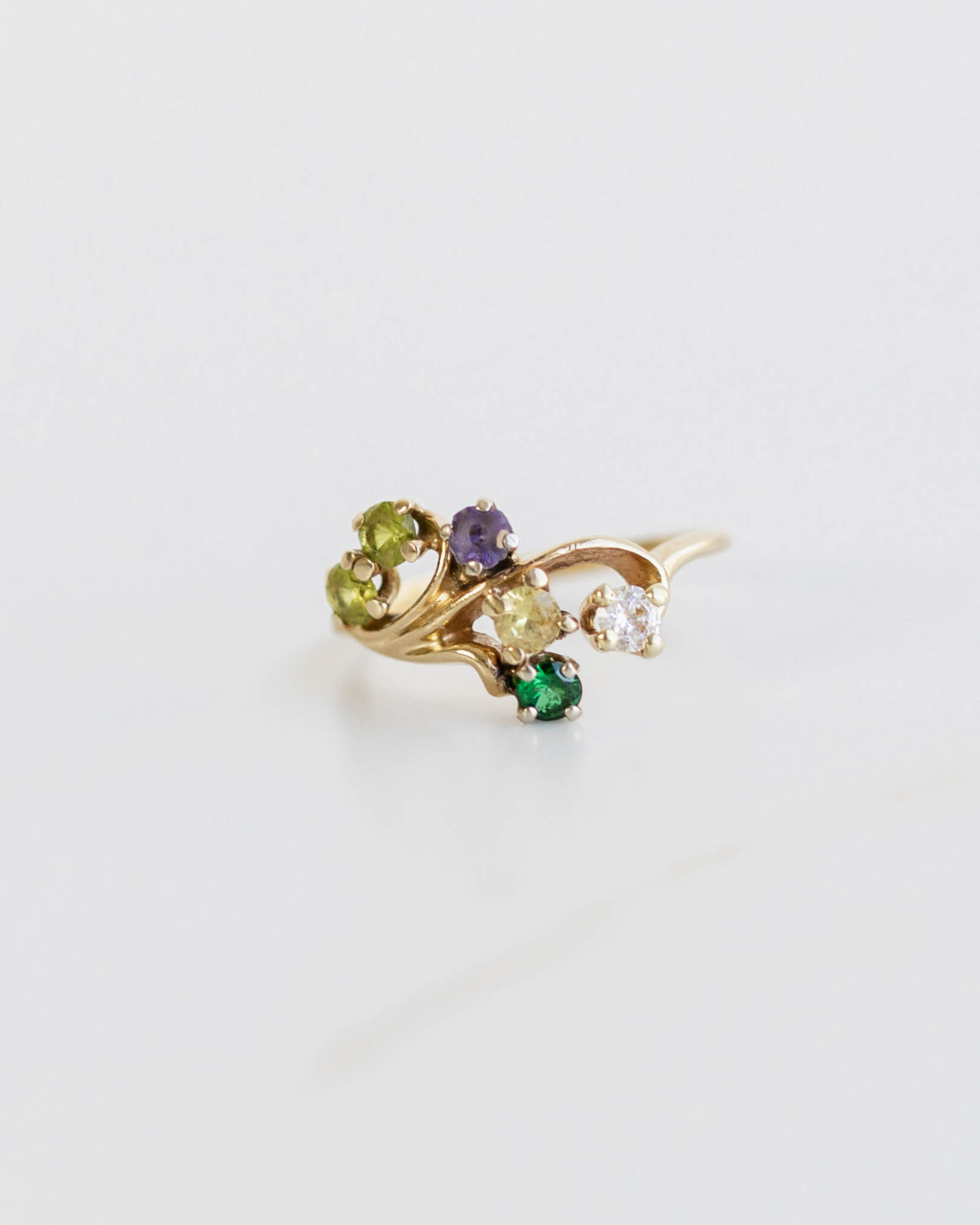 Gold ring with green and purple gemstones on a light gray background