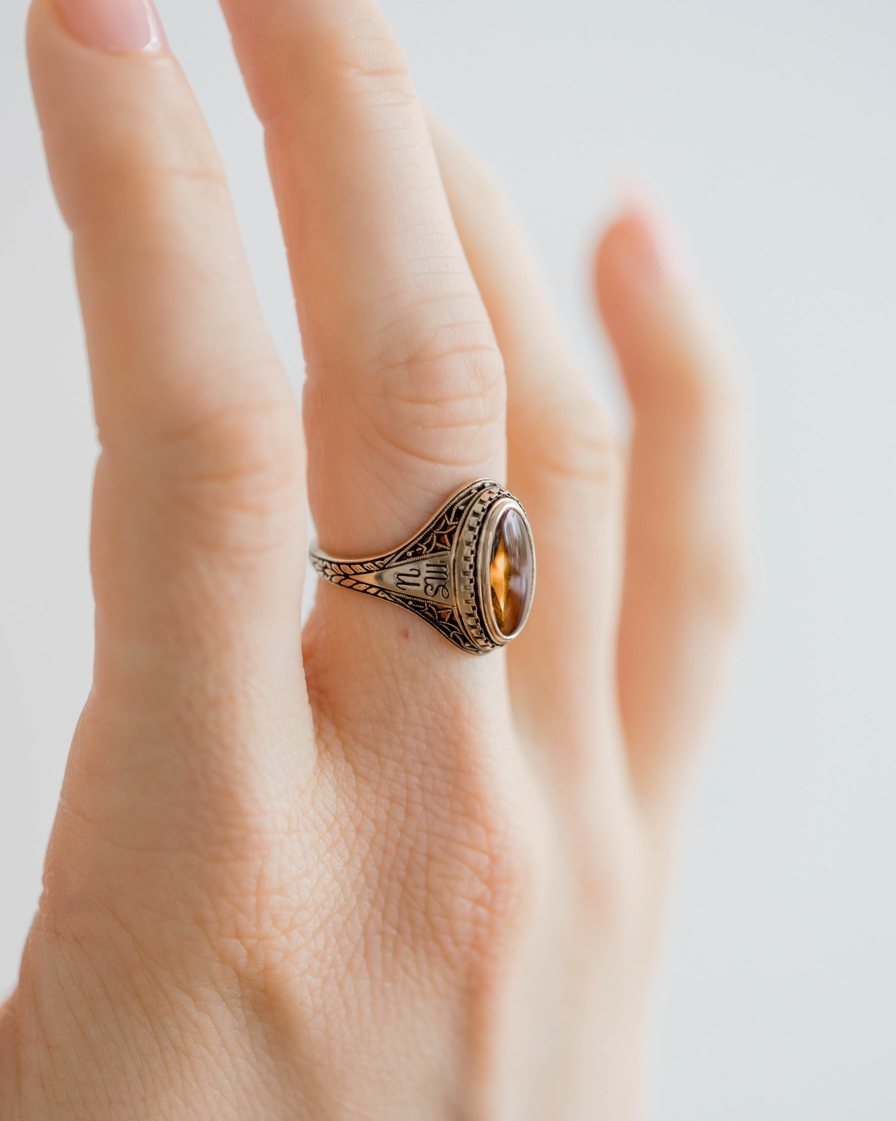 Close-up of a hand wearing a decorative ring with a clear gemstone on a light background