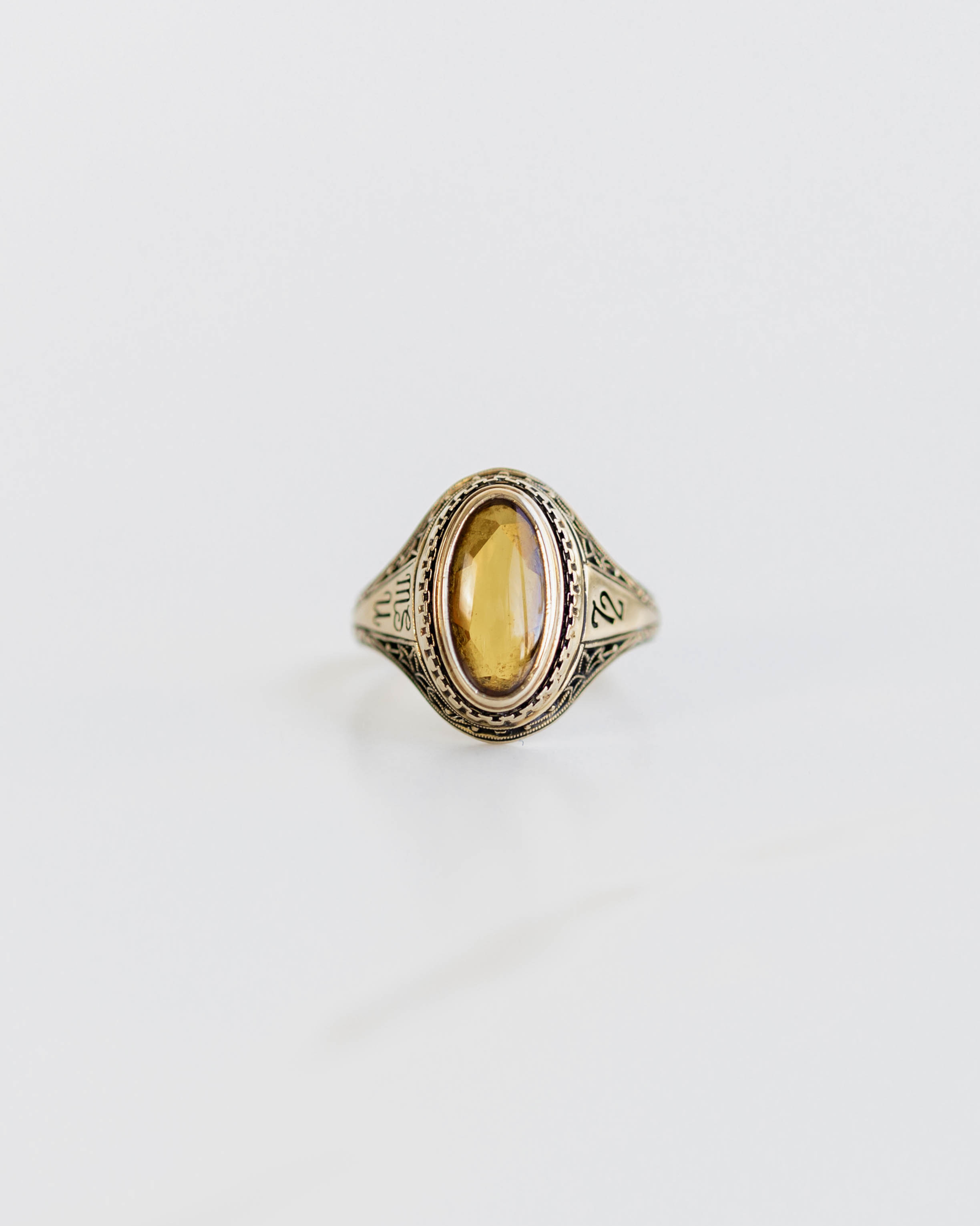 Gold ring with a yellow gemstone on a light gray background