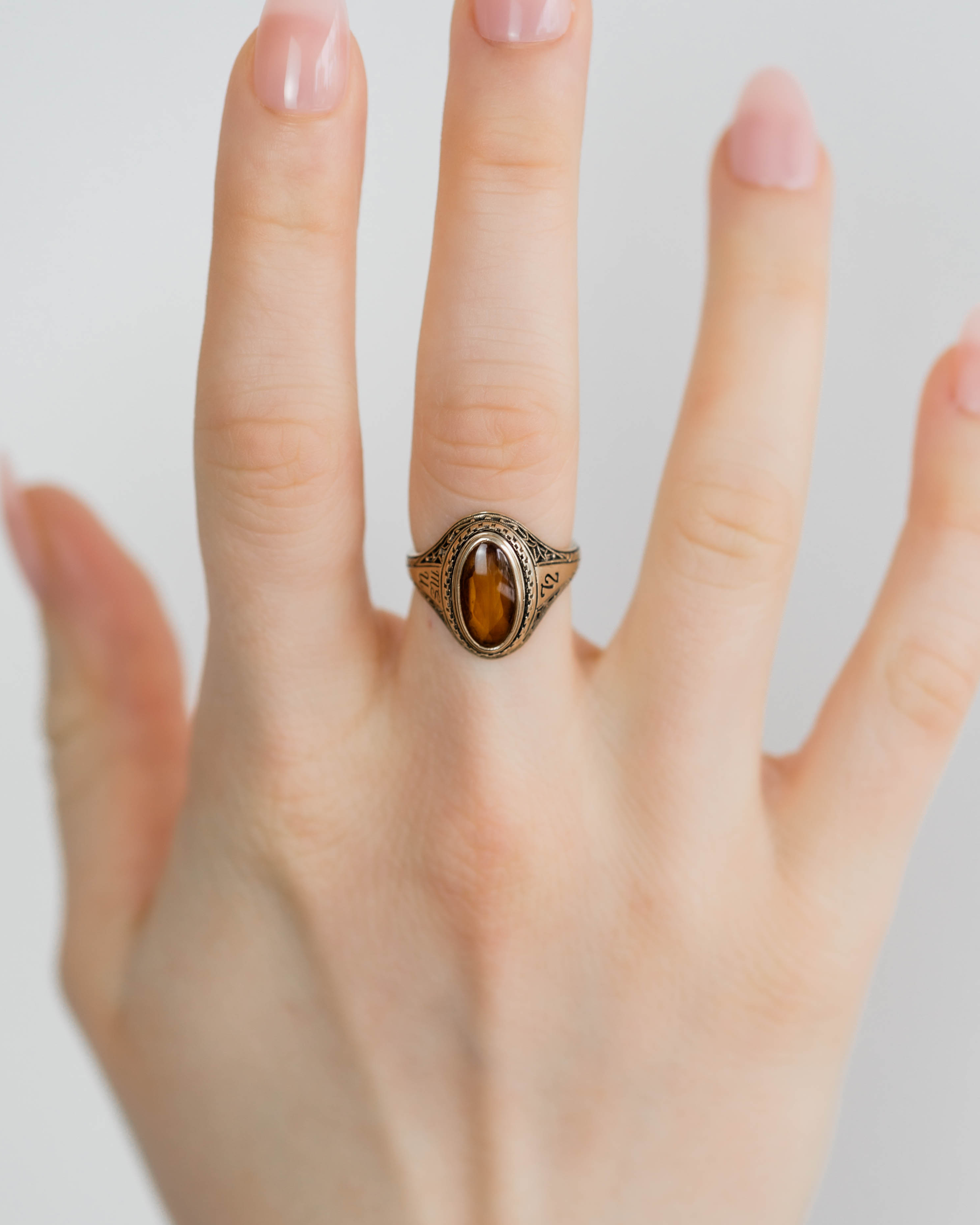 Hand wearing a gold ring with a brown gemstone on a light background