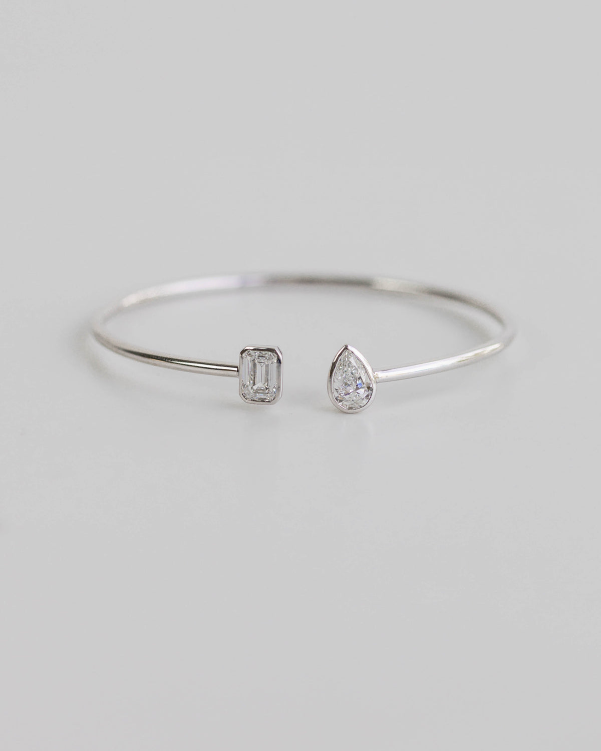 Silver open bangle with two gemstones on a light gray background